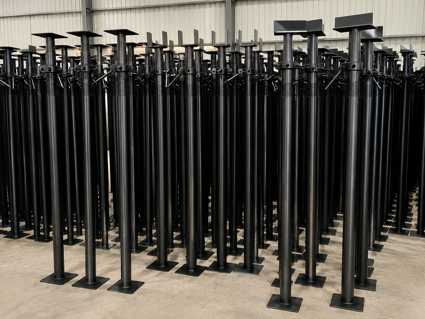 Bulk adjustable steel props stored in a warehouse for construction slab support and formwork applications.